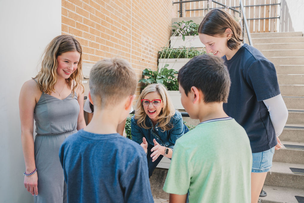 Robyn kneeling down surrounded by teens and kids talking directly to two boys